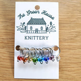 translucent red, orange, yellow, green, light blue, dark blue, purple and white glass bead ring-style stitch markers in the rainbow colourway with silver wire